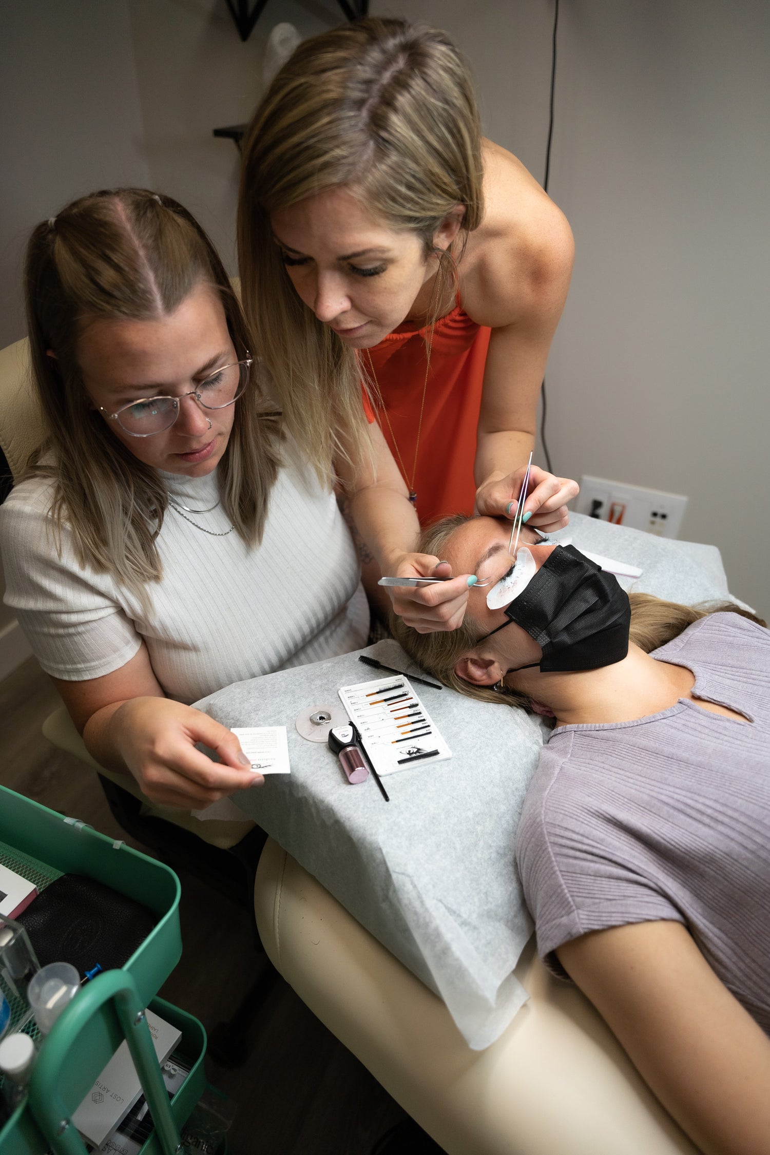 2 woman performing eyelash extension procedure and looking into materials for the procedure